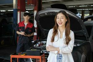 joven asiático hembra cliente con automotor mecánico obrero, brazos cruzado y contento sonrisas en calidad a mantenimiento cochera, profesional vehículo Servicio estación, reparar cheque y reparar auto industria. foto