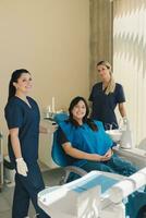 Portrait of three women, dentist, assistant and patient in a dental office smiling and looking at camera. photo