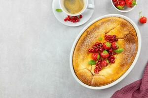 Homemade casserole with cottage cheese, semolina, fresh red currant and strawberry on light gray background. Top view. Copy space. photo