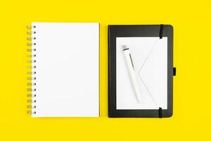 Modern office workplace flat lay with blank paper notebook mockup, envelope and pen on yellow background. Top view. Copy space. photo
