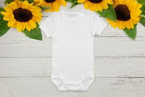 White baby girl or boy bodysuit mockup flat lay with sunflowers on white wooden background. Design onesie template, print presentation mock up. Top view. photo
