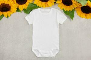 White baby girl or boy bodysuit mockup flat lay with sunflowers on gray concrete background. Design onesie template, print presentation mock up. Top view. photo