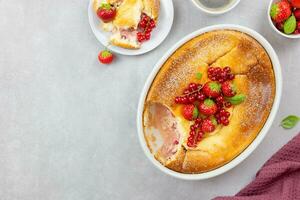 Homemade casserole with cottage cheese, semolina, fresh red currant berries and strawberry on light gray background. Top view. Copy space. photo