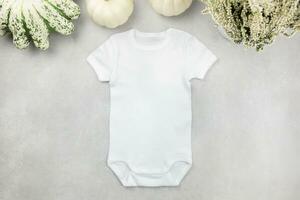 White baby girl or boy bodysuit mockup flat lay with pumpkins on gray concrete background. Design onesie template, print presentation mock up. Top view. photo