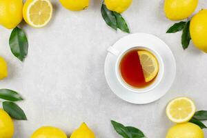 Cup of tea with fresh lemons and leaves on light gray concrete background. Hot healthy beverage. Immune defence, vitamin c. Top view. Copy space. photo