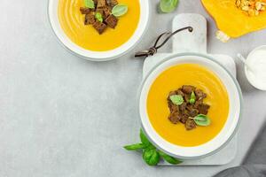 Seasonal autumn roasted pumpkin and carrot soup with cream and rye bread croutons on a light concrete background. Top view. Copy space. photo
