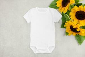 White baby girl or boy bodysuit mockup flat lay with sunflowers on gray concrete background. Design onesie template, print presentation mock up. Top view. photo