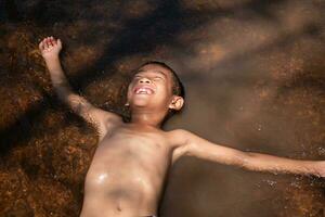 Asian young boy smile cute and charming play in the water happily and have fun.young asian boy floating on the surface of the water on the background flowing water and soft sunlight a fresh feeling. photo