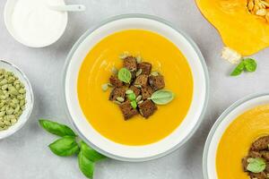 Seasonal autumn roasted pumpkin and carrot soup with cream and rye bread croutons on a light concrete background. Top view. photo