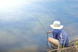 Asian young boy fishing by river using bamboo fishing rod on beautiful water surface and sunrise,Lifestyle of asian children,Lifestyle in rural Thailand,Concept of life and sustainability. photo