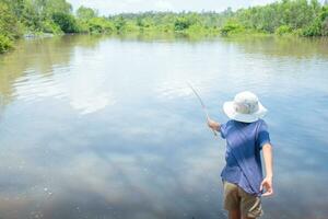 Asian boy standing fishing by river using bamboo fishing rod on beautiful water surface and sunrise ,Lifestyle of asian children,Lifestyle in rural Thailand,Concept of life and sustainability. photo