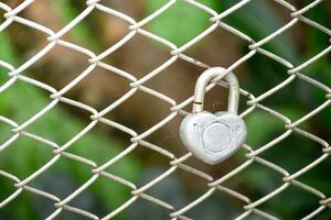 Heart shape keychain and wire metal fence net on the blurry forest background,two keychains are hanging. photo