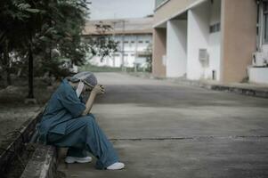 Tired depressed female asian scrub nurse wears face mask blue uniform sits on hospital floor,Young woman doctor stressed from hard work photo