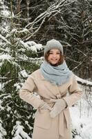 un linda niña es en pie debajo el nieve en el bosque en mitones y un Saco foto