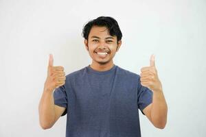 Young handsome asian man wearing casual with white background doing happy thumbs up gesture with hand. Approving expression looking at the camera showing success. photo