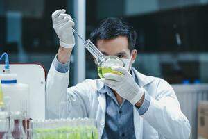 Scientist man research biotechnology from herbal plants for pharmaceutical and cosmetic product development. The experiment uses dropper to add reagents into bottle flask to detect active compounds. photo