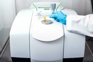 Hand of scientist using a stainless spatula to scoop sample solid from vial to the Fourier Transform Infrared Spectroscopy FTIR pedestal instrument for substance analysis and chemical characterization photo
