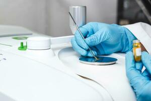 Hand of scientist using a stainless spatula to scoop sample solid from vial to the Fourier Transform Infrared Spectroscopy FTIR pedestal instrument for substance analysis and chemical characterization photo