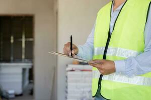 el inspector o ingeniero está inspeccionando la construcción y el aseguramiento de la calidad de la nueva casa usando una lista de verificación. ingenieros o arquitectos o contratistas trabajan para construir la casa antes de entregársela al propietario foto