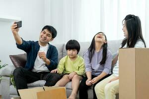 Moviente casa, reubicación familia sonrisa y jugar juntos después moverse a nuevo hogar, dentro el habitación estaba un cartulina caja Contiene personal pertenencias y mueble. moverse en el nuevo departamento, condominio foto