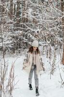 linda niña en un Saco y sombrero caminando en un Nevado bosque foto