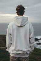 Back view of young man in white hoodie looking at the ocean photo