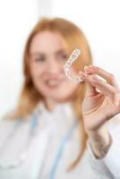 Dental care.Smiling girl with red hair holding heart shaped aligners photo