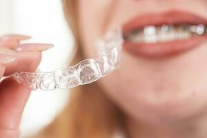 Dental care.Smiling girl with braces on her teeth holds aligners in her hands and shows the difference between them photo