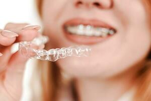 Dental care.Smiling girl with braces on her teeth holds aligners in her hands and shows the difference between them photo