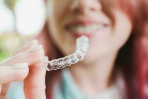 Dental care.Smiling girl with braces on her teeth holds aligners in her hands and shows the difference between them photo