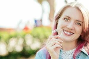 Dental care.Smiling girl with braces on her teeth holds aligners in her hands and shows the difference between them photo