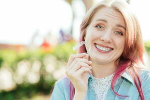 Dental care.Smiling girl with braces on her teeth holds aligners in her hands and shows the difference between them photo