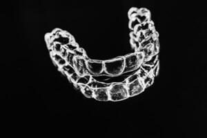 Invisible dental teeth brackets tooth aligners on black background. Plastic braces dentistry retainers to straighten teeth. photo