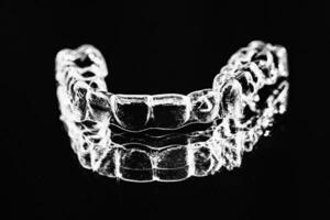 Invisible dental teeth brackets tooth aligners on black background. Plastic braces dentistry retainers to straighten teeth. photo