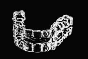 Invisible dental teeth brackets tooth aligners on black background. Plastic braces dentistry retainers to straighten teeth. photo