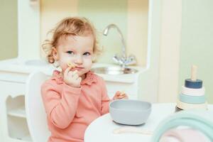 pequeño bebé come pasta en el para niños cocina foto