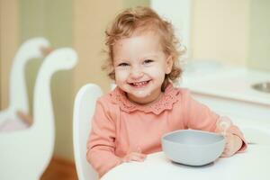 riendo y alegre bebé niña come pasta en el cocina foto