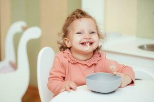 riendo y alegre bebé niña come pasta en el cocina foto