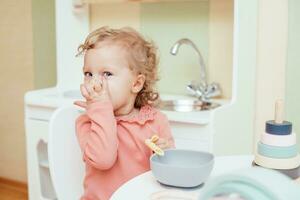 contento pequeño niña comiendo pasta en jardín de infancia foto