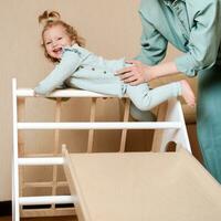 A little girl climbs a wooden slide in the gym. The child goes in for sports and develops photo