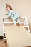 A little girl climbs a wooden slide in the gym. The child goes in for sports and develops photo