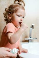 alegre y gracioso niña cepillado su dientes en el Mañana foto