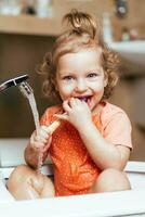 Happy laughing baby girl brushing her teeth in the bath photo