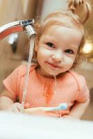 linda y gracioso bebé niña cepillado su dientes en el Mañana en el bañera foto