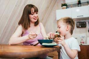 Cheerful child eating pasta in the kitchen with mom photo