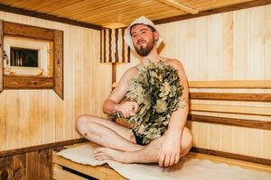 un hombre con un Escoba en su mano es relajante en el sauna foto