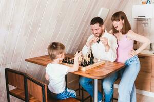 Pregnant mom watching dad and son play chess at the table photo