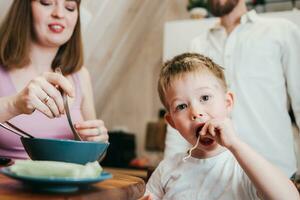 contento niño come pasta en el cocina con su familia foto
