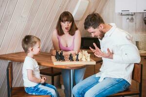 contento familia madre, papá y su hijo jugando ajedrez en el habitación foto