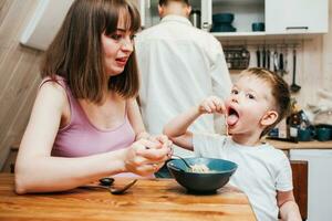 Mother with father feeding the child in the kitchen with pasta photo